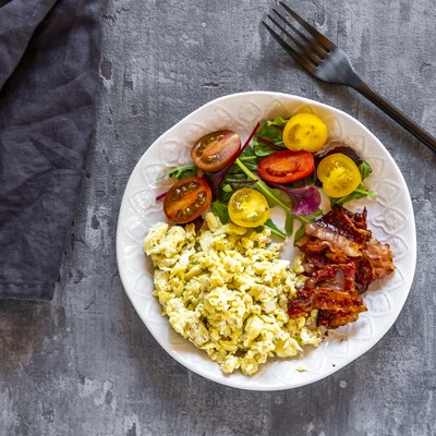 Scrambled eggs with fried bacon and salad with tomato, low carb, from above