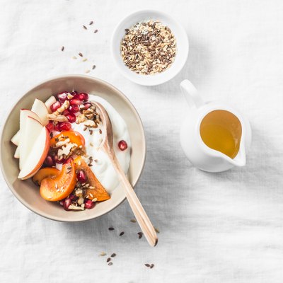 Full fruit and greek yogurt breakfast bowl. Persimmon, apple, walnuts, pomegranates and natural yogurt. Healthy food concept on light background, top view
