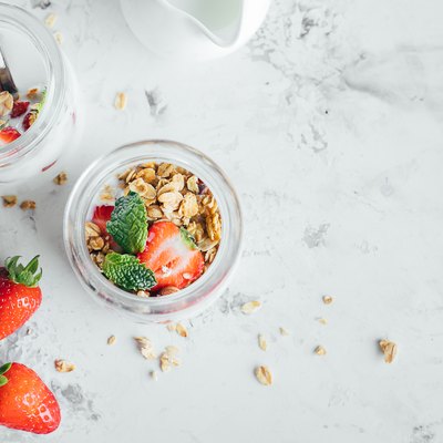 Two jars with tasty parfaits made of granola, strawberries and yogurt on white marble table. Top view, copy space