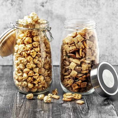 Two jars with caramelized popcorn and snack mix on gray background