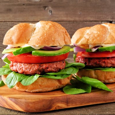 Plant based meatless burgers with avocado, tomato and spinach against a wood background