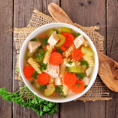 Homemade chicken noodle soup with vegetables, top view on a wood background