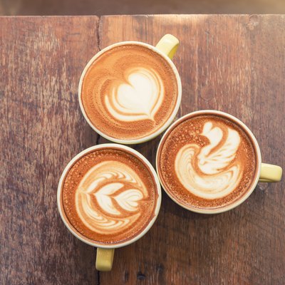 Top view of three cups of coffee in yellow cups with various types of latte art