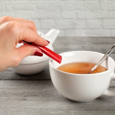 Detail on woman hand pouring sugar from small packet into cup of hot tea.