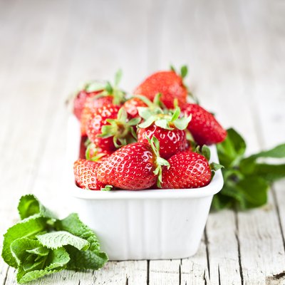 Fresh red strawberries in white bowl and mint leaves on rustic wooden background.
