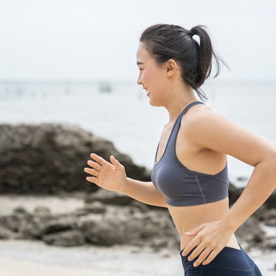 Young Asian woman running on the beach. Girl jogging workout in seaside