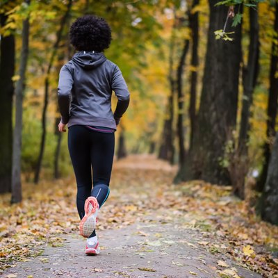 Young woman jogging through the fall park, rear shot.