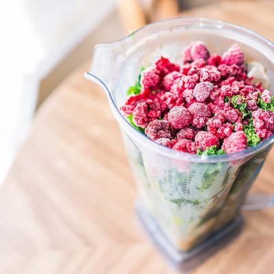 Macro closeup of fresh green kale and frozen raspberries in plastic blender container for smoothie