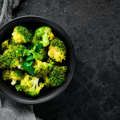 Boiled broccoli in a black plate. On a black background. Top view. Free space for your text.
