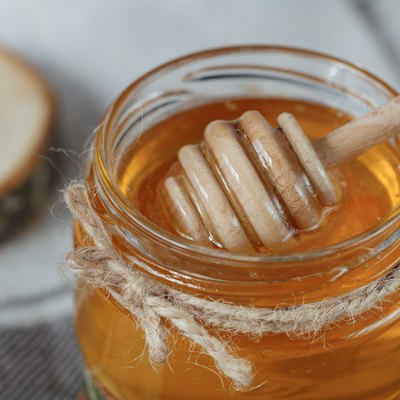Glass pot of honey on a rustic bacground.