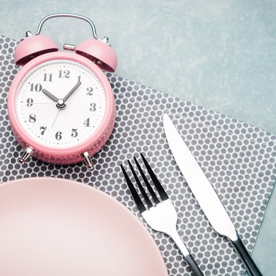 Alarm clock and plate with cutlery. Concept of intermittent fasting, lunchtime, diet and weight loss