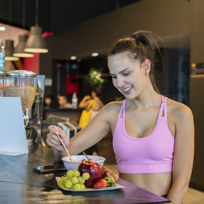 Beautiful young woman eating a healthy bowl and a red apple and more fruit at the gym