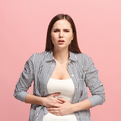 The stomach ache. The sad woman with stomach ache or pain on a pink studio background