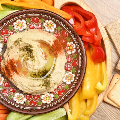 A plate of hummus with olive oil, spices and vegetables.