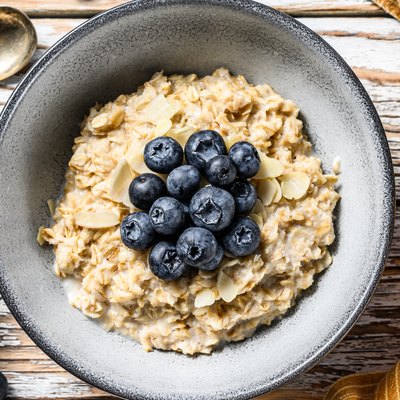 Breakfast oatmeal with blueberries and almonds. White wooden background. Top view