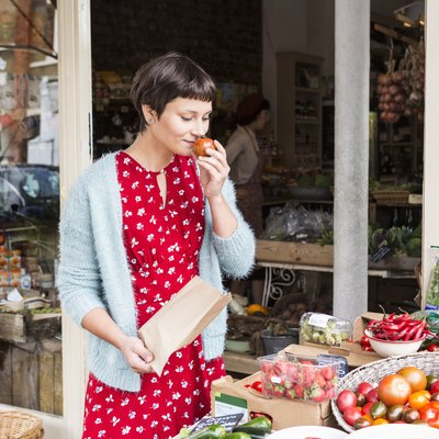 Woman smelling fresh tomato at organic farm shop.