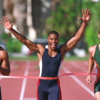 portrait of a young male athlete crossing the finish line first with his arms raised up in victory