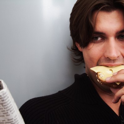 Young man reading newspaper eating bread and cheese