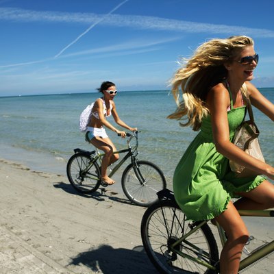 Three young woman riding bicycles on beach, laughing, side view