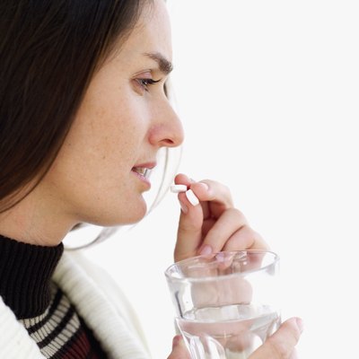 Side profile of a young woman taking a pill and holding a glass of water