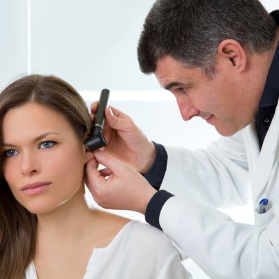 Doctor ENT checking ear with otoscope to woman patient
