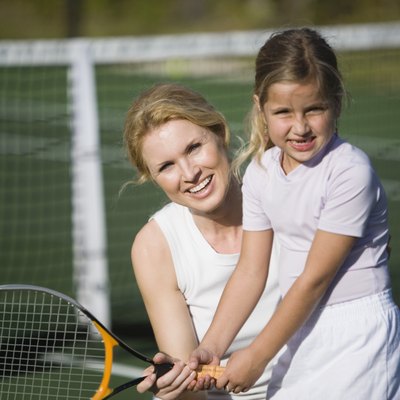 Mother teaching daughter how to play tennis