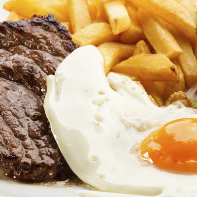 Beefsteak, fried egg, French fries and vegetables