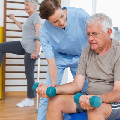 Female therapist assisting senior man with dumbbells
