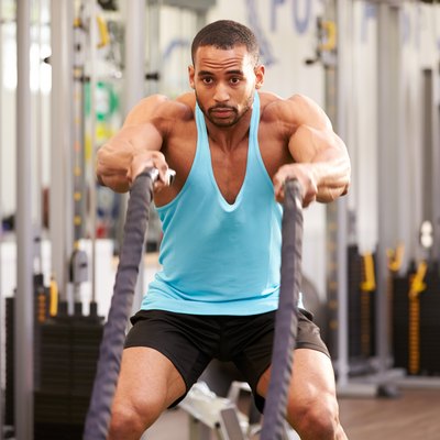 Young man working out with battle ropes at a gym