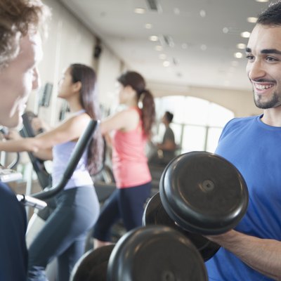 Two young men smiling and lifting weights in the gym