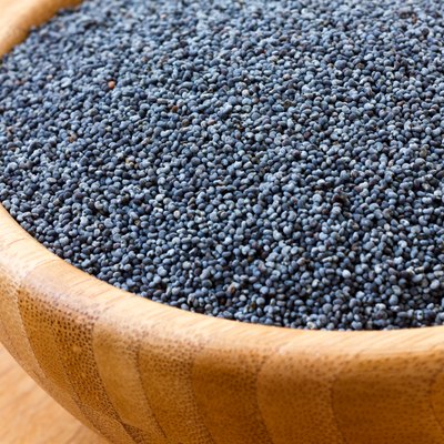 Detail of poppy seeds in wood bowl on wood surface.