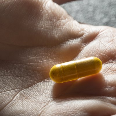 Bare hand holding one yellow medicinal tablet
