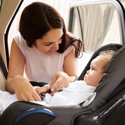 Mother Putting Baby Son Into Car Travel Seat