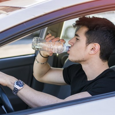 Young man driving car and drinking water from bottle