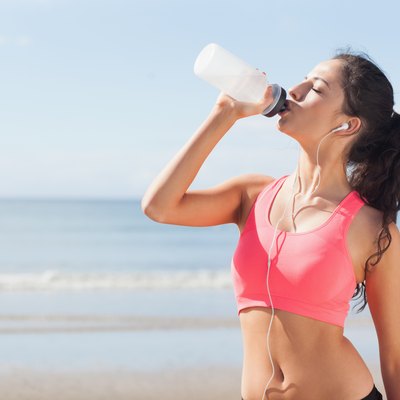 Beautiful healthy woman drinking water on beach