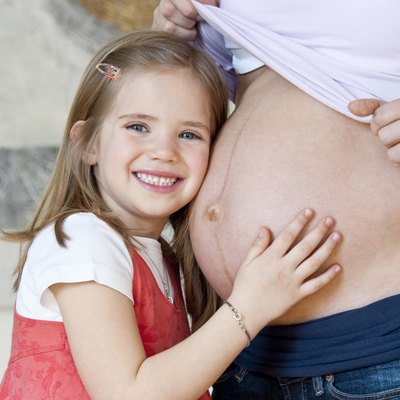Daughter listening to pregnant mid adult mothers belly, smiling