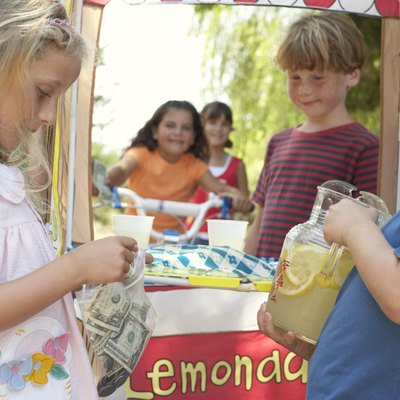 Children (6-12) at lemonade stall, girl (5-7) putting money in bag