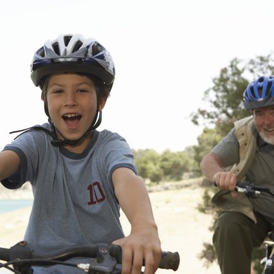 Grandson (5-7) and grandfather riding bikes, portrait (focus on boy)