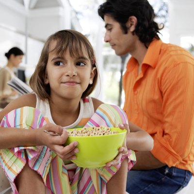 Family at breakfast table, girl (8-10) holding bow of cereal