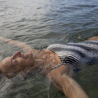 Senior woman floating in pool, arms outstretched, smiling, close-up