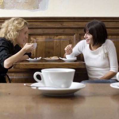 Two young women with coffee in cafe, smiling