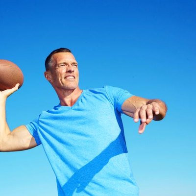 Confident mature man throwing American football against clear blue sky