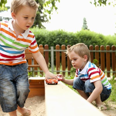 Twin brothers playing in sandpit with toy cars