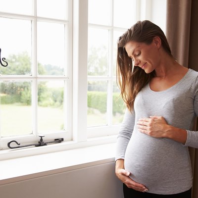 Pregnant Woman Standing By Window Holding Belly