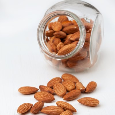 Almond nuts in a glass jar on white wooden background.