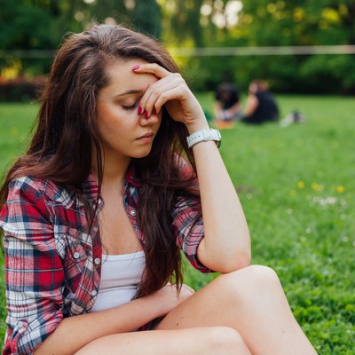 Girl sitting in park with headache. What a terrible day.
