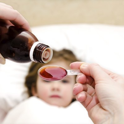 Mother pouring medication in a spoon in the foreground
