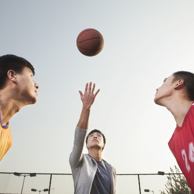 Referee throwing ball in the air, basketball players getting ready for a jump