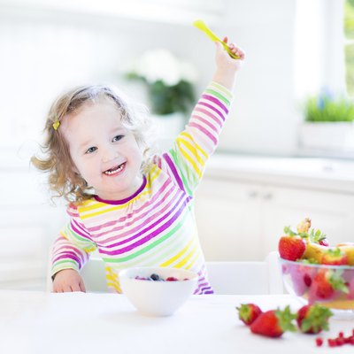 Toddler girl with curly hair wearing colorful shirt having breakfast