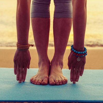 Young woman doing yoga exercise on beach near the sea at sunset in summer, face is not visible